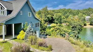 A two-story house with a garage, surrounded by a lush garden and a lake. - Blue Heron Point, Lakefront Luxury - Views, Party Deck, Docks, Hot Tub & FirePit (Moneta)