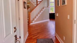 A hallway with wooden flooring, white walls, a staircase with wooden railings, and a ceiling light fixture. - Blue Heron Point, Lakefront Luxury - Views, Party Deck, Docks, Hot Tub & FirePit (Moneta)