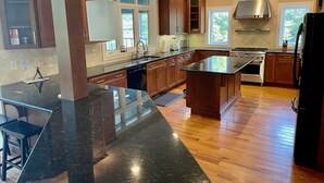 A modern kitchen with wooden cabinets, a large island, and a stainless steel range hood. - Blue Heron Point, Lakefront Luxury - Views, Party Deck, Docks, Hot Tub & FirePit (Moneta)