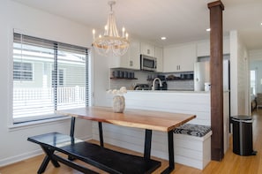 A modern kitchen with white cabinetry, a wooden dining table, and a chandelier.