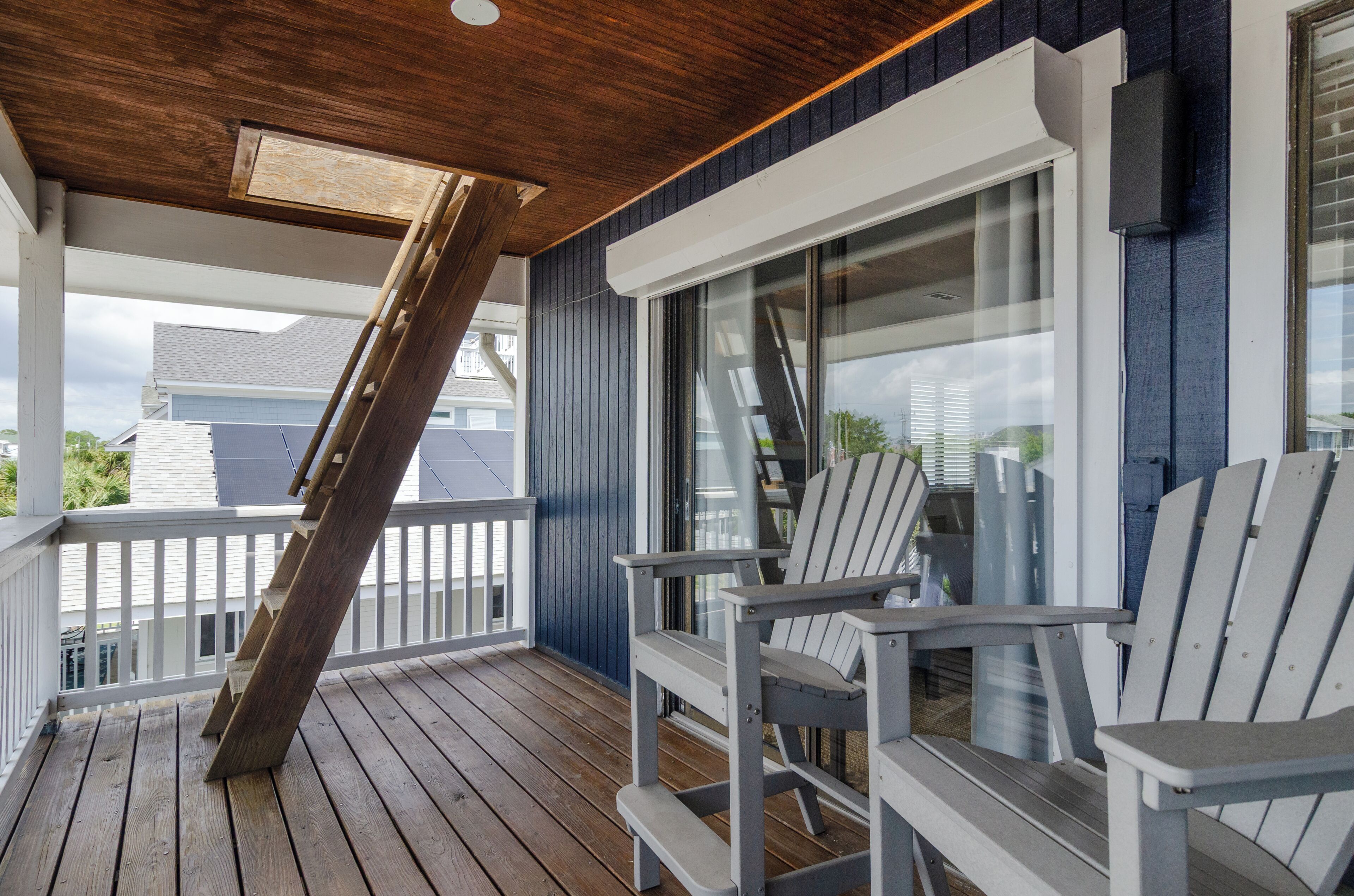 Eine Holzterrasse mit Adirondack-Stühlen, einer Glastür und einem weißen Geländer.