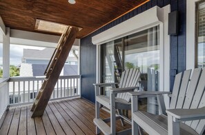 Een houten terras met Adirondack stoelen, een glazen deur en een witte balustrade.