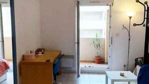 Una stanza con un letto, una scrivania, una sedia, un tavolo, una pianta in vaso e una lampada.