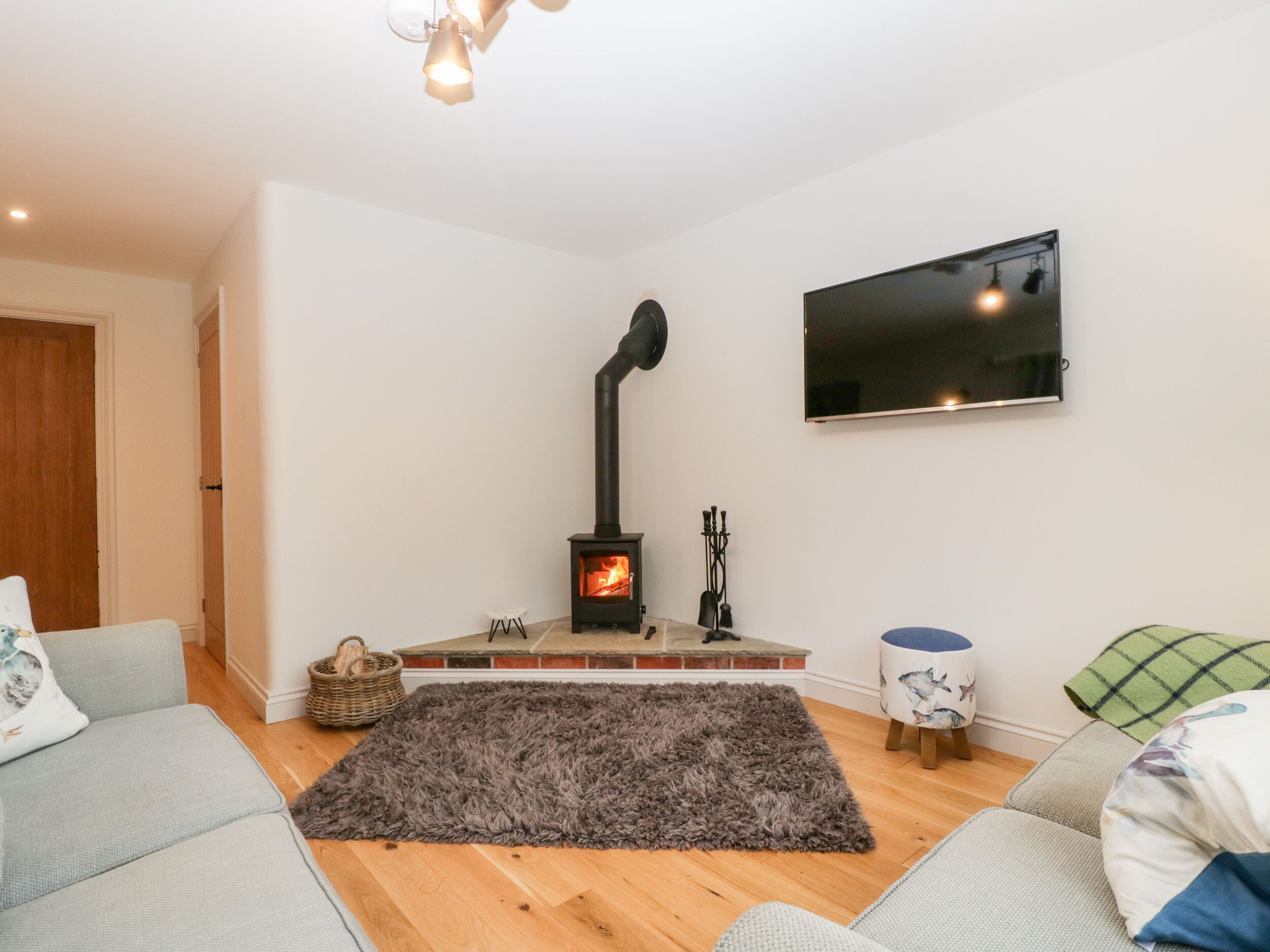 Ett vardagsrum med en vedeldad kamin, en platt-TV och en grå, lurvig matta.