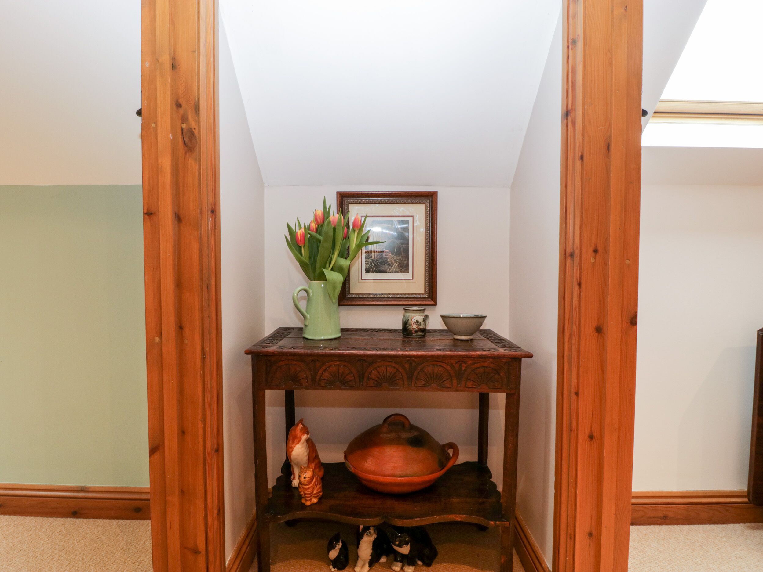 A corner room with a wooden table, a framed picture, and a vase of flowers.