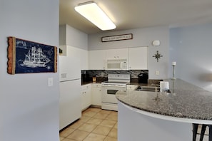 A modern kitchen with white cabinets, a granite countertop, and a microwave.
