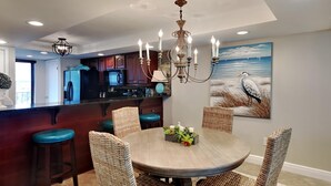 A dining area with a round table, wicker chairs, and a chandelier. - Edgewater Tower III #612 | Gulf Views, Lagoon Pool, Near Area Fun! (Panama City Beach)