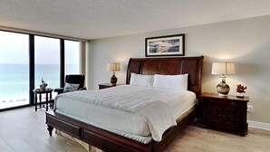 A spacious bedroom with a large bed, two bedside tables with lamps, a wooden headboard, and a large window offering a view of the ocean. - Edgewater Tower III #612 | Gulf Views, Lagoon Pool, Near Area Fun! (Panama City Beach)