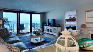 A spacious living room with a large sliding glass door leading to a balcony, a television, and a white cabinet. - Edgewater Tower III #612 | Gulf Views, Lagoon Pool, Near Area Fun! (Panama City Beach)