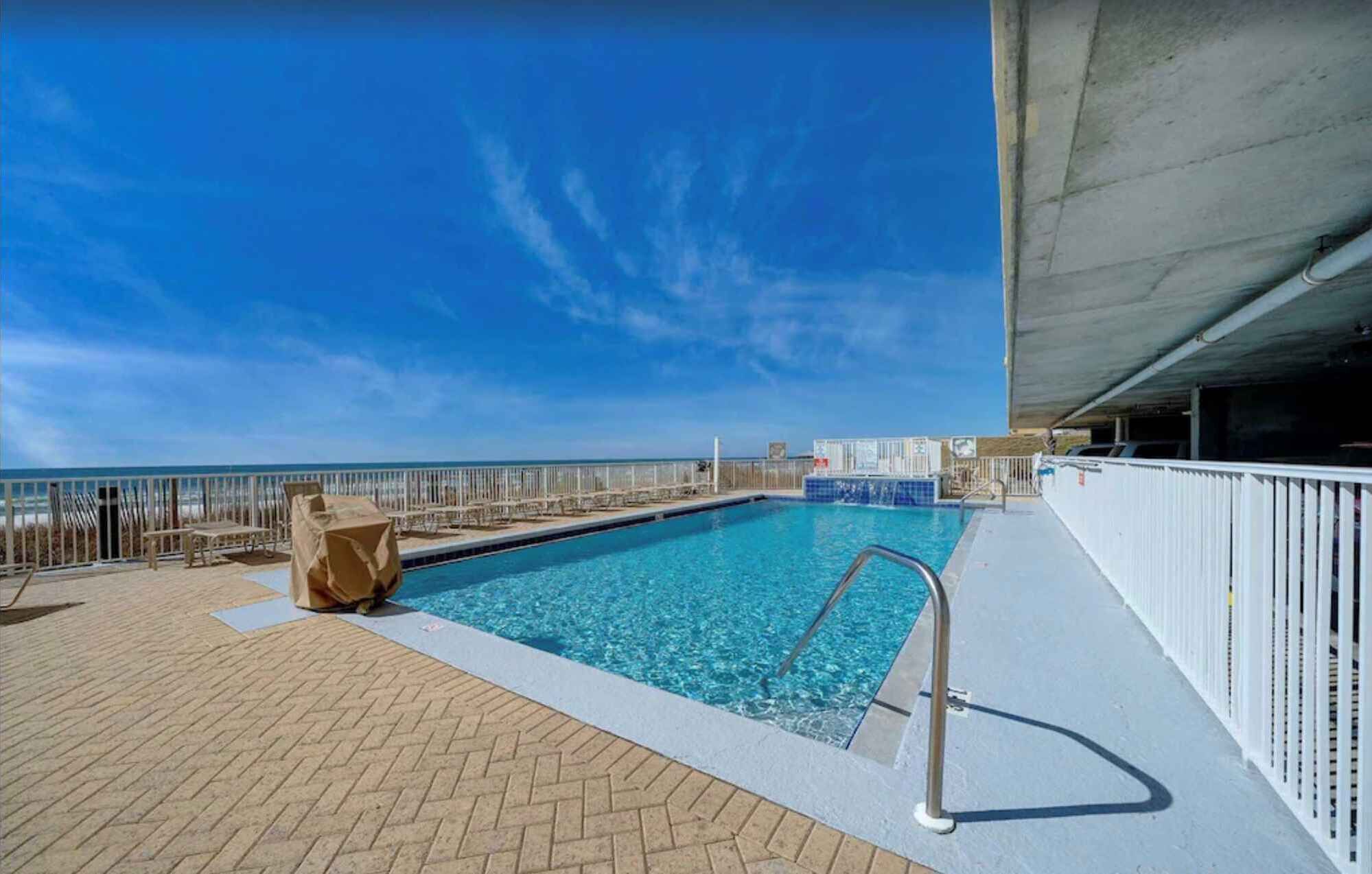 A pool area with a clear view of the ocean, a lifeguard stand, and a covered section.
