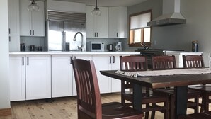 A modern kitchen with white cabinets, stainless steel appliances, and a wooden dining table with chairs. - Pigeon Lake Luxury close to town of Bobcaygeon (Kawartha Lakes)