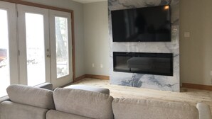 A living room with a large flat-screen TV mounted on a marble wall, a fireplace below it, and a grey sofa. - Pigeon Lake Luxury close to town of Bobcaygeon (Kawartha Lakes)