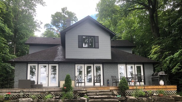 A two-story house with a large front porch, stone retaining wall, and a grill area. - Pigeon Lake Luxury close to town of Bobcaygeon (Kawartha Lakes)