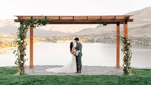 Une cérémonie de mariage avec une pergola en bois et des décorations florales, le tout au bord d’un lac.