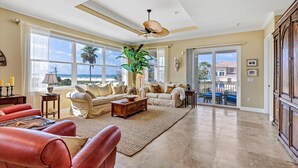 Ein großzügiges Wohnzimmer mit großem Fenster, Deckenventilator und Blick auf den Strand.