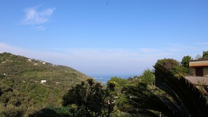 Vista de um morro com céu limpo, um corpo d'água ao longe e edifícios espalhados.