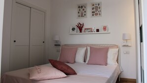 Quarto com cama, paredes brancas, luminária no teto e uma porta.