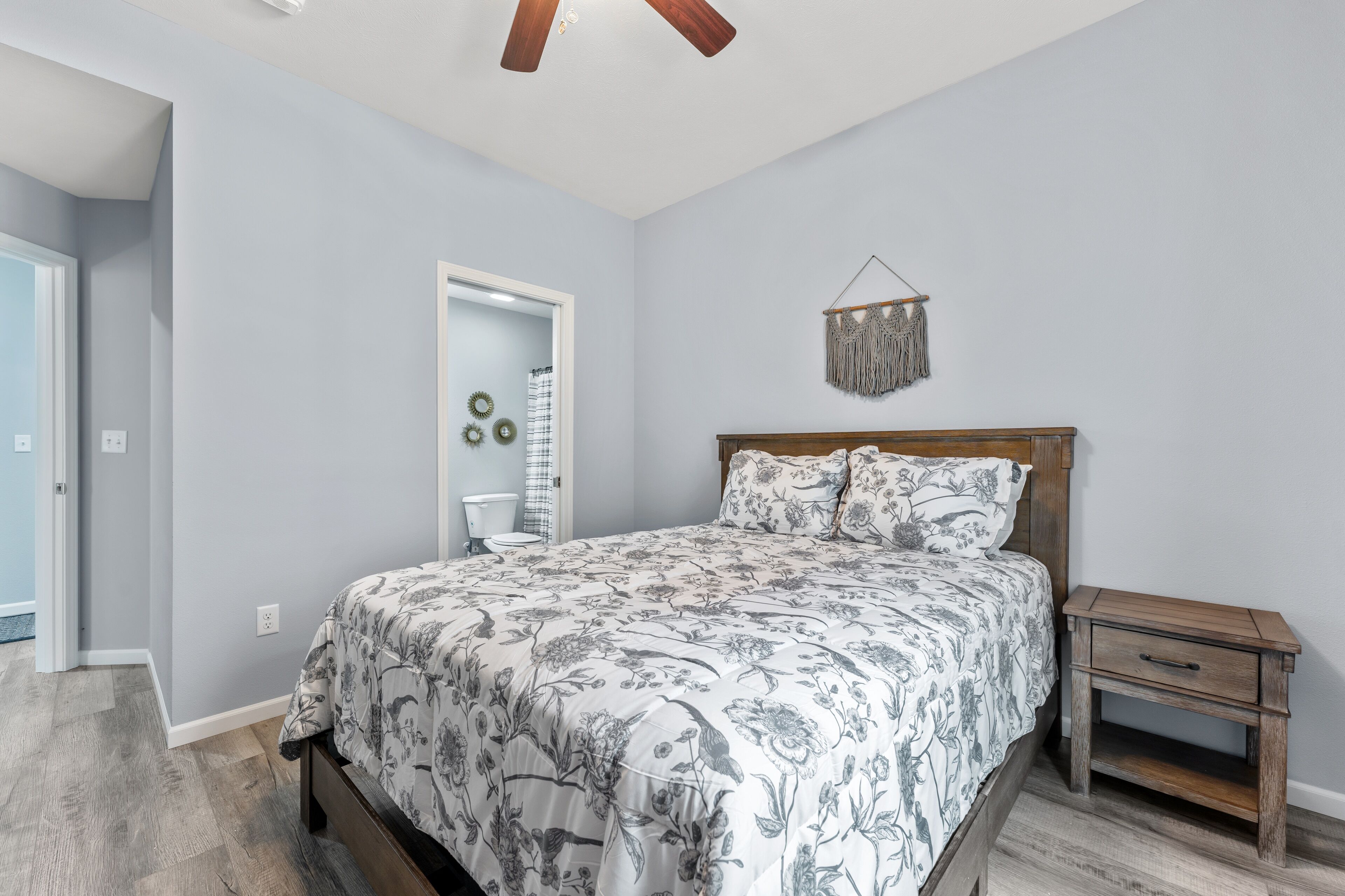 A bedroom with a bed, wooden nightstand, and a ceiling fan.