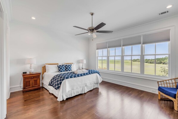 A bedroom with a large window, a bed, a nightstand, and a ceiling fan.