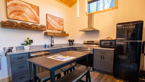 A modern kitchen with granite countertops, a black refrigerator, stainless steel appliances, and a dining area with a bench. - Legends Lane A - Hosted by The Chalets (Logan)