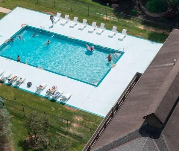 Vista aérea de una piscina rectangular con varias pistas, rodeada de sillones blancos y una zona de césped.