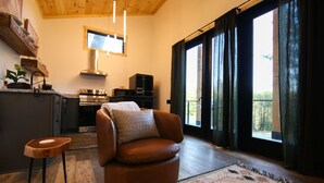 A living room with a brown leather sofa, a wooden coffee table, and a large window with curtains. - Legends Lane A - Hosted by The Chalets (Logan)