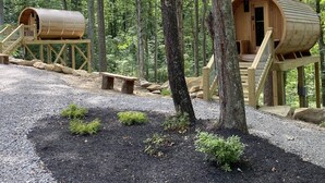Deux cabanes cylindriques en bois, dotées d’escaliers en bois, entourées d’une forêt.