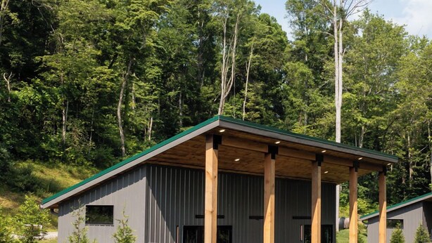 Une cabane moderne dotée d’un patio couvert, entourée d’une végétation luxuriante et d’arbres.