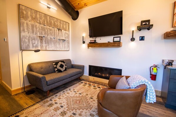 A living room with a sofa, a fireplace, a television, and a mounted artwork.