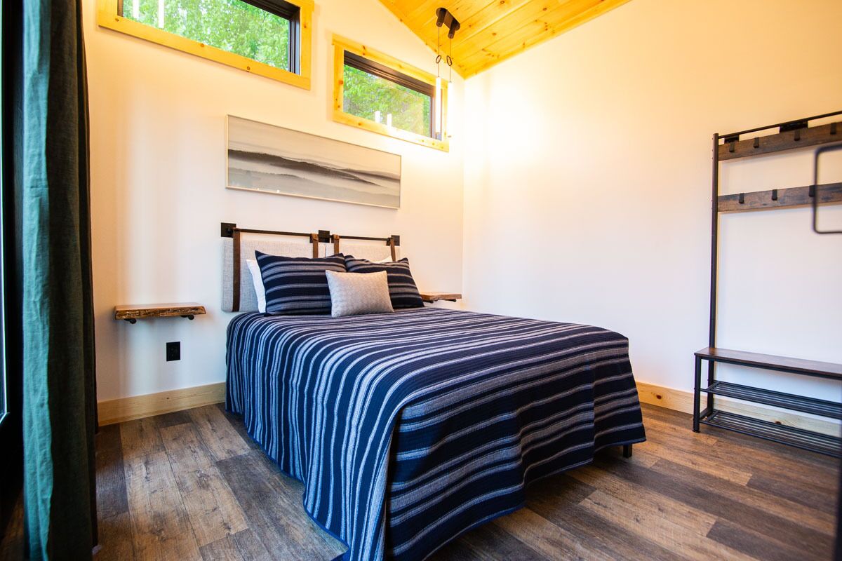 A bedroom with a bed, wooden flooring, a window, and a bunk bed structure.