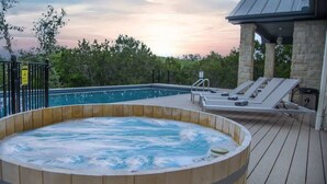 A hot tub on a wooden deck with lounge chairs, a pool, and a stone building in the background. - Spicewood Lodge w/Pool, HotTub (Spicewood)
