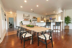 A spacious dining area with a wooden table and chairs, a kitchen in the background, and a potted plant.