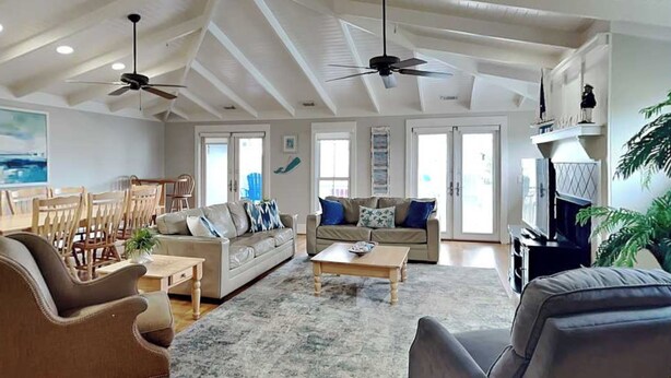 A spacious living room with high ceilings, ceiling fans, a fireplace, and a large window. - Partial beach view home w. shared pool + private elevator. (Tybee Island)