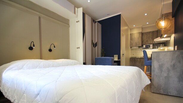 A modern hotel room with a large bed, a kitchenette, and a dining area. - Huellas Botique Aparments (Posadas)