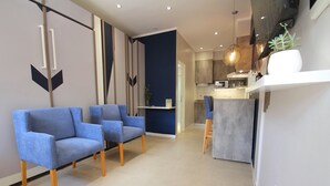 A modern living area with two blue armchairs, a kitchen with a bar area, and a dining space. - Huellas Botique Aparments (Posadas)