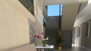 A sunlit outdoor area with a beige sofa, a small table with a potted plant, and patterned flooring. - Huellas Botique Aparments (Posadas)