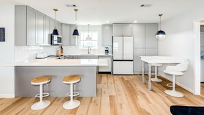 Una cocina moderna con armarios grises, una isla blanca con taburetes, un refrigerador y luces colgantes.