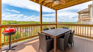 A covered outdoor deck with a wooden table and chairs, a barbecue grill, and a view of the surrounding landscape. - Walk In Level, Family Friendly, Relaxing New Condo in Stonebridge Resort. (Branson West)