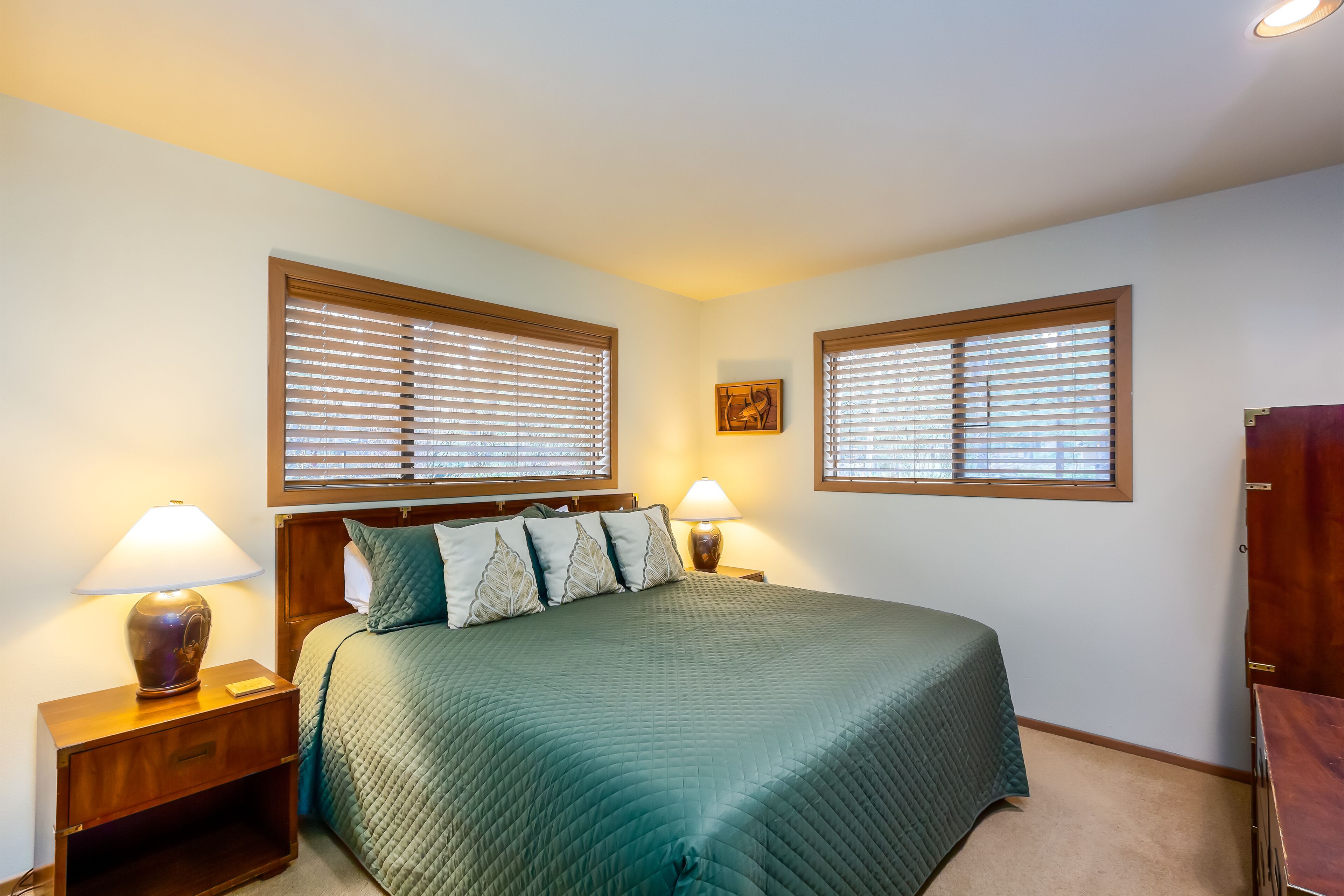 Un dormitorio con una cama, dos lámparas de noche, una mesita de noche y dos ventanas con persianas.
