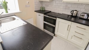 A kitchen with white cabinets, a black countertop, a stove, a dishwasher, and a kettle.