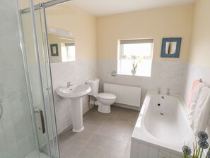 A bathroom with a glass shower enclosure, a sink, a toilet, a bathtub, and a window with a plant. - 22 Town Place (Ballinrobe)