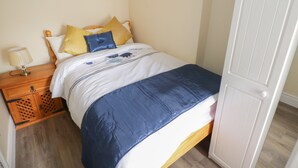 A neatly made bed with a blue and white duvet, a wooden nightstand with a lamp, and a wooden floor.
