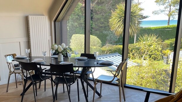 A dining area with a table set for four, large windows offering a view of a garden and the sea. - Maison du Rocher Plat - Vue Mer - Proche Plage - 4 (Saint-Jacut-de-la-Mer)