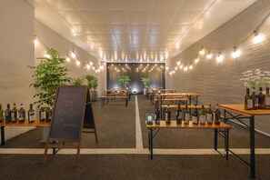 Un espacio interior moderno con mesas, bancos, plantas en macetas y botellas de vino.