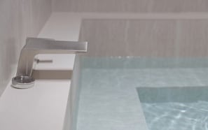 Un baño moderno con grifo cromado, lavamanos blanco y bañera con mampara de vidrio.
