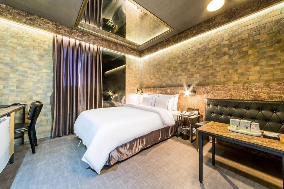 A hotel room with a bed, a desk, a chair, a table with amenities, and a mirror.