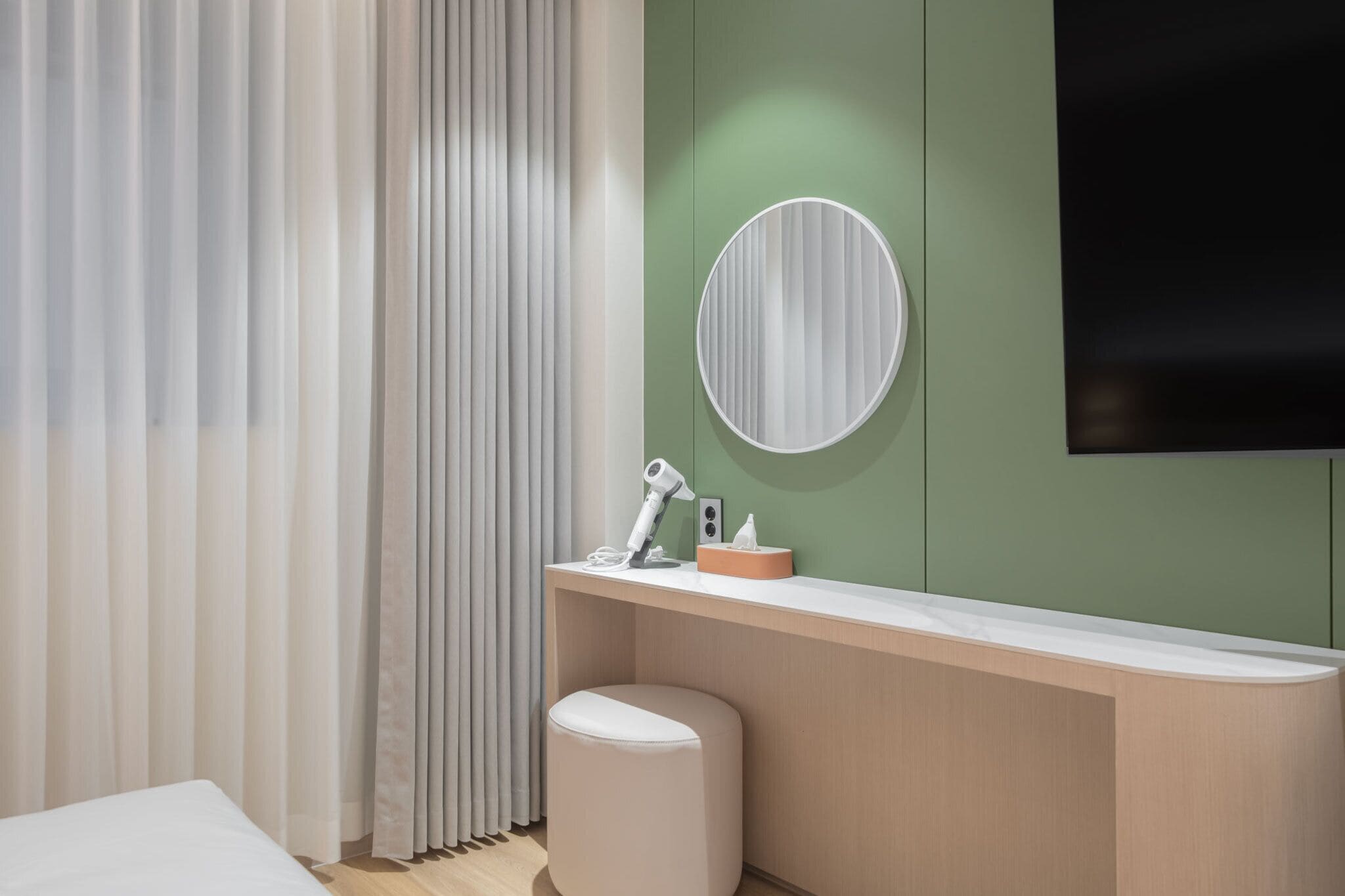 A modern bathroom with a vanity, a round mirror, a hairdryer, and a towel on a stool.