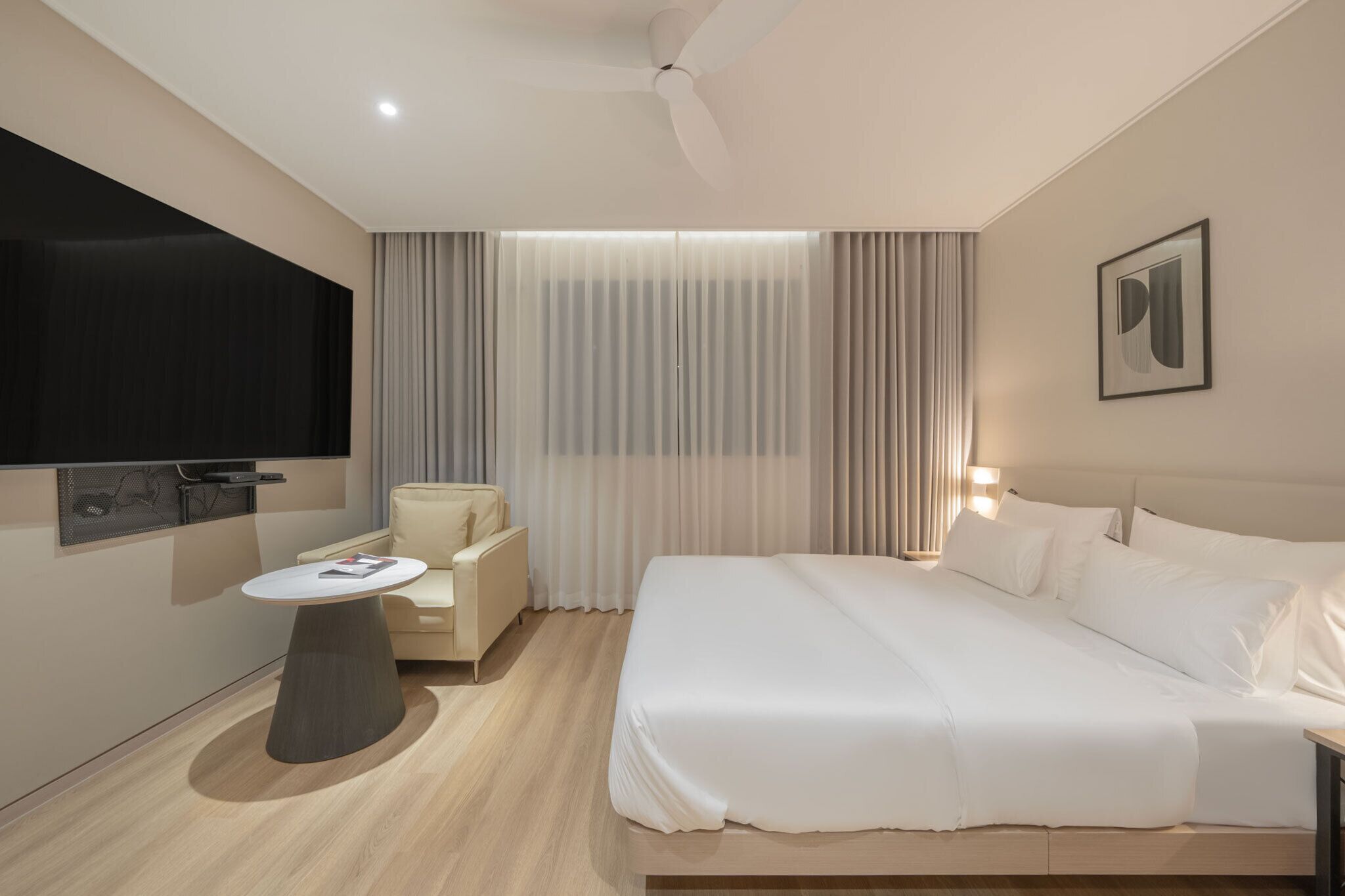 A modern hotel room with a bed, a desk, a chair, a TV, and curtains.