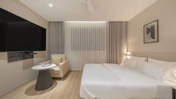 A modern hotel room with a bed, a desk, a chair, a TV, and curtains.