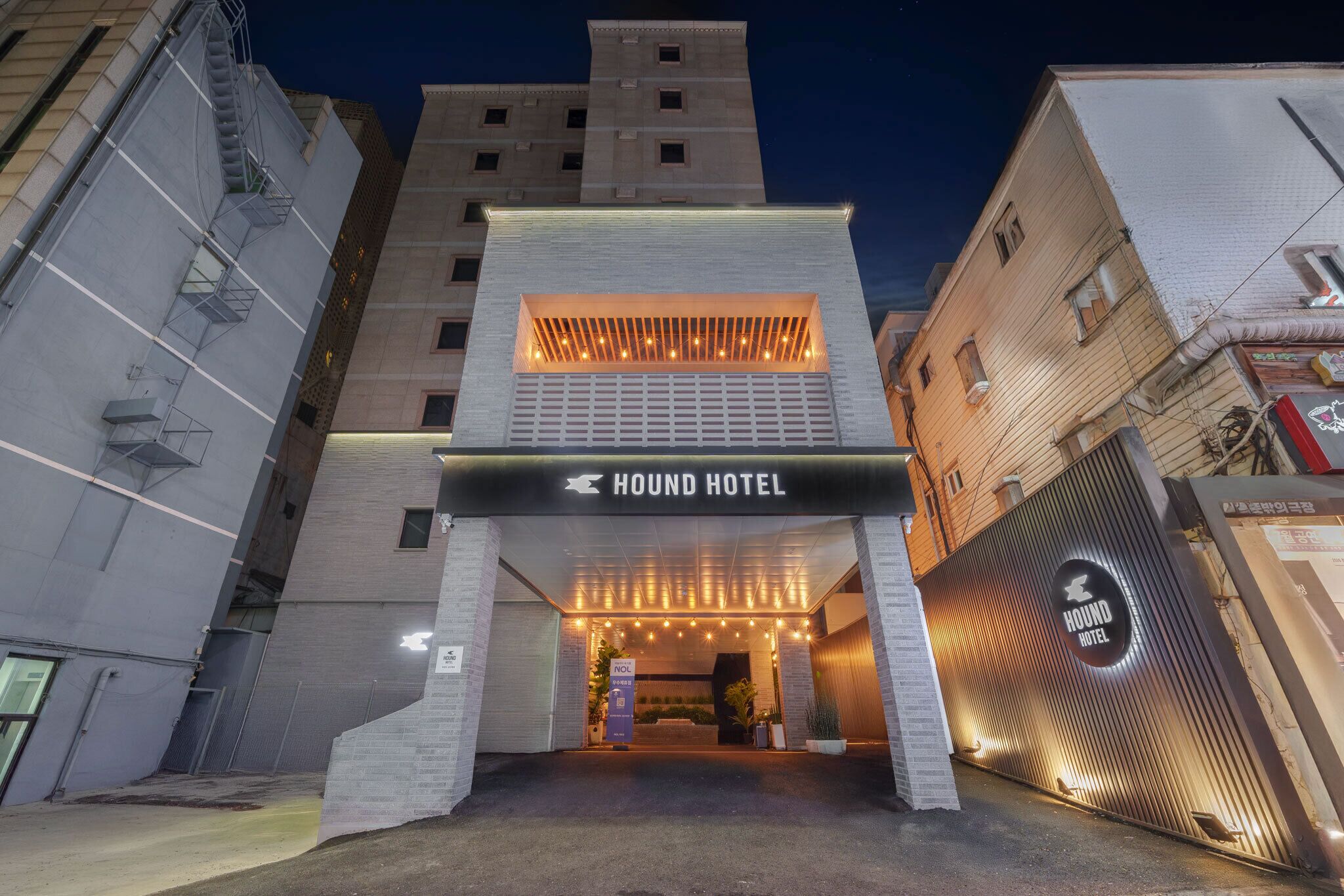 A hotel entrance with a sign reading 'HOUND HOTEL,' a modern design, and a gated driveway.